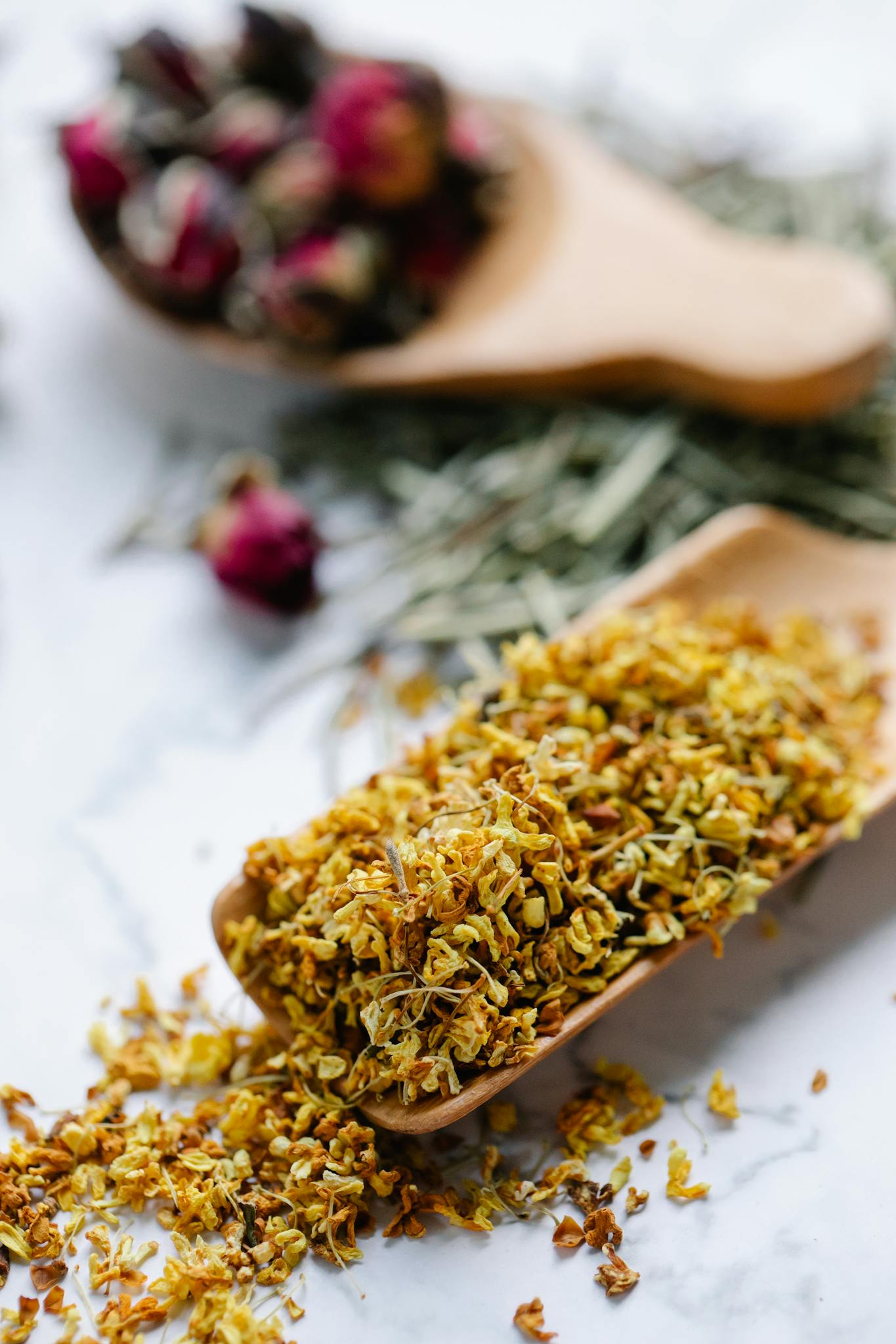A close-up of dried herbal ingredients on wooden spoons, perfect for tea.