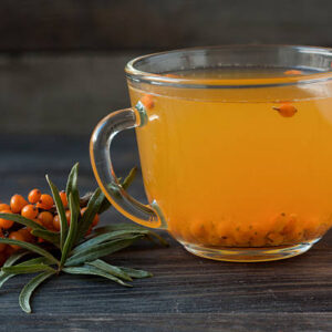 Tea of sea buckthorn berries with branch on dark wooden background.
