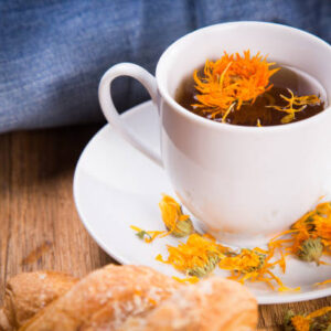 Fresh tea with croissant and calendula on wooden background